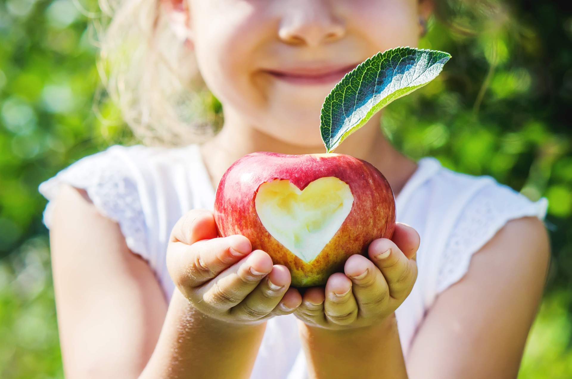 Ein Kind mit einem Apfel, auf dem ein Herz abgebildet ist.
