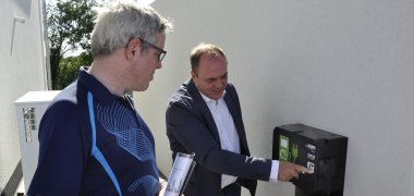 „Nachhaltigkeit muss kein Schlagwort bleiben“ Markus Müllers, Geschäftsführender Gesellschafter der MKM BauProjekte GmbH erläutert Landrat Christian Engelhardt die Ladestation für Elektrofahrzeuge bei einem Wohnhaus im Energie- und Wohnpark Helfrichsgärtel III in Biblis.