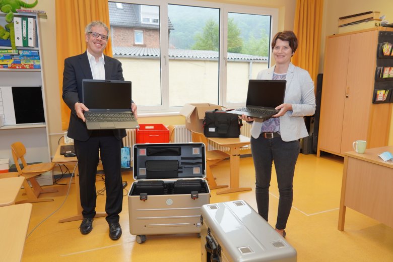 Landrat Christian Engelhardt und Melanie Sauer, Schulleiterin der Grundschule Elmshausen, freuen sich über die neue technische Ausstattung der Bergsträßer Schulen. Beide stehen mit Laptops in der Hand in einem Klassenzimmer.