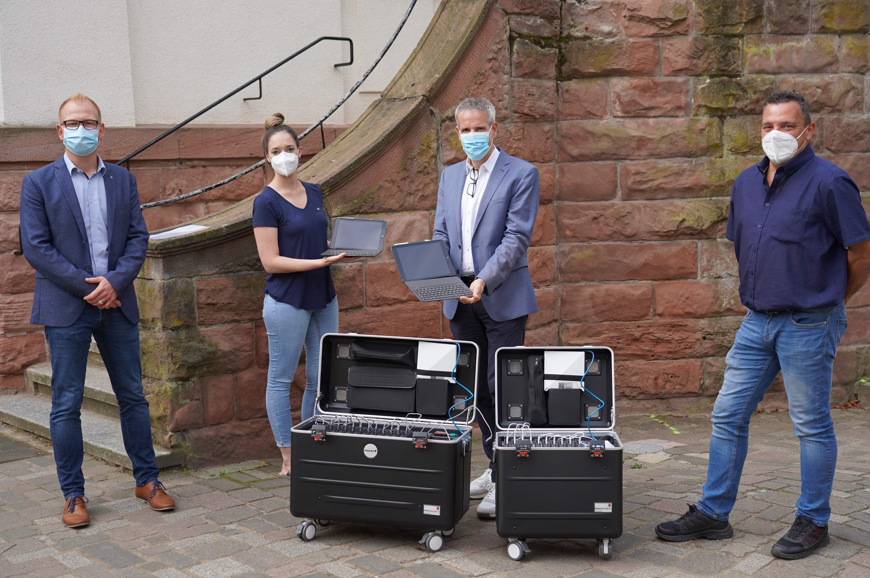 Zu sehen sind vier Personen, drei Männern, eine Frau. Die beiden Personen in der Mitte, die Frau und Landrat Engelhardt halten schwarze iPads in den Händen. Vor Ihnen sind schwarze, aufgeklappte Boxen auf Rollen zu sehen.