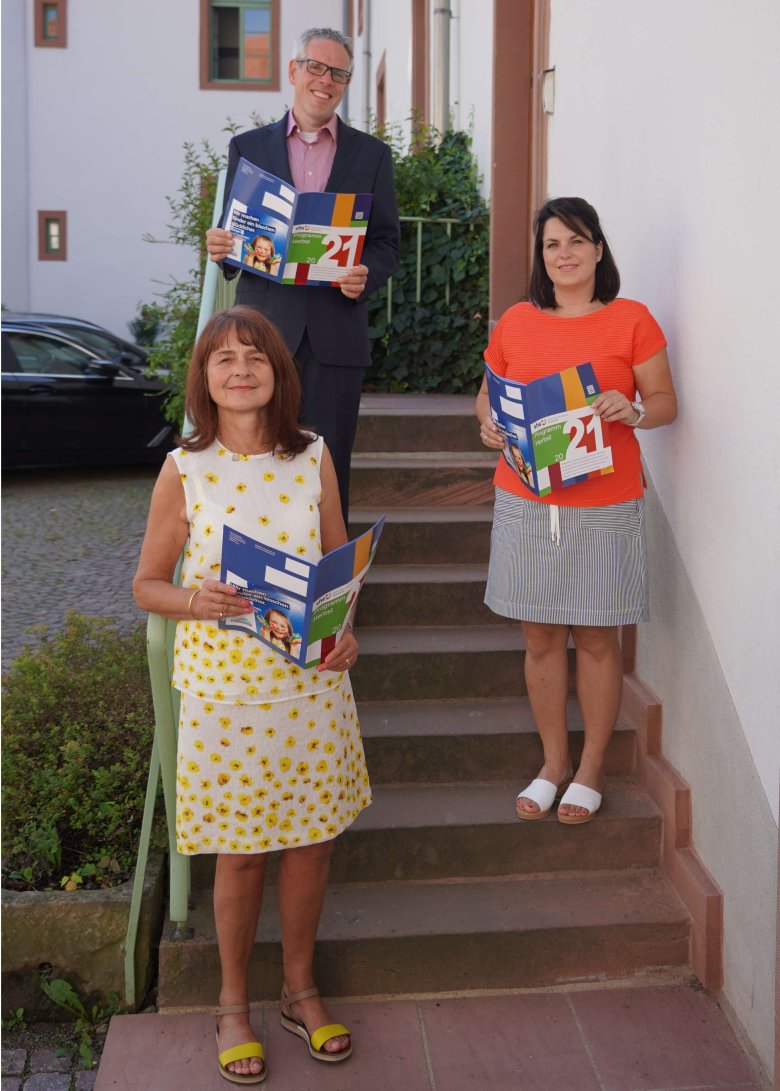 Landrat Christian Engelhardt steht mit Iris Hoch und Melanie Knauf  auf einer Treppe. Alle drei halten das neue Programm der Kreisvolkshochschule in den Händen.