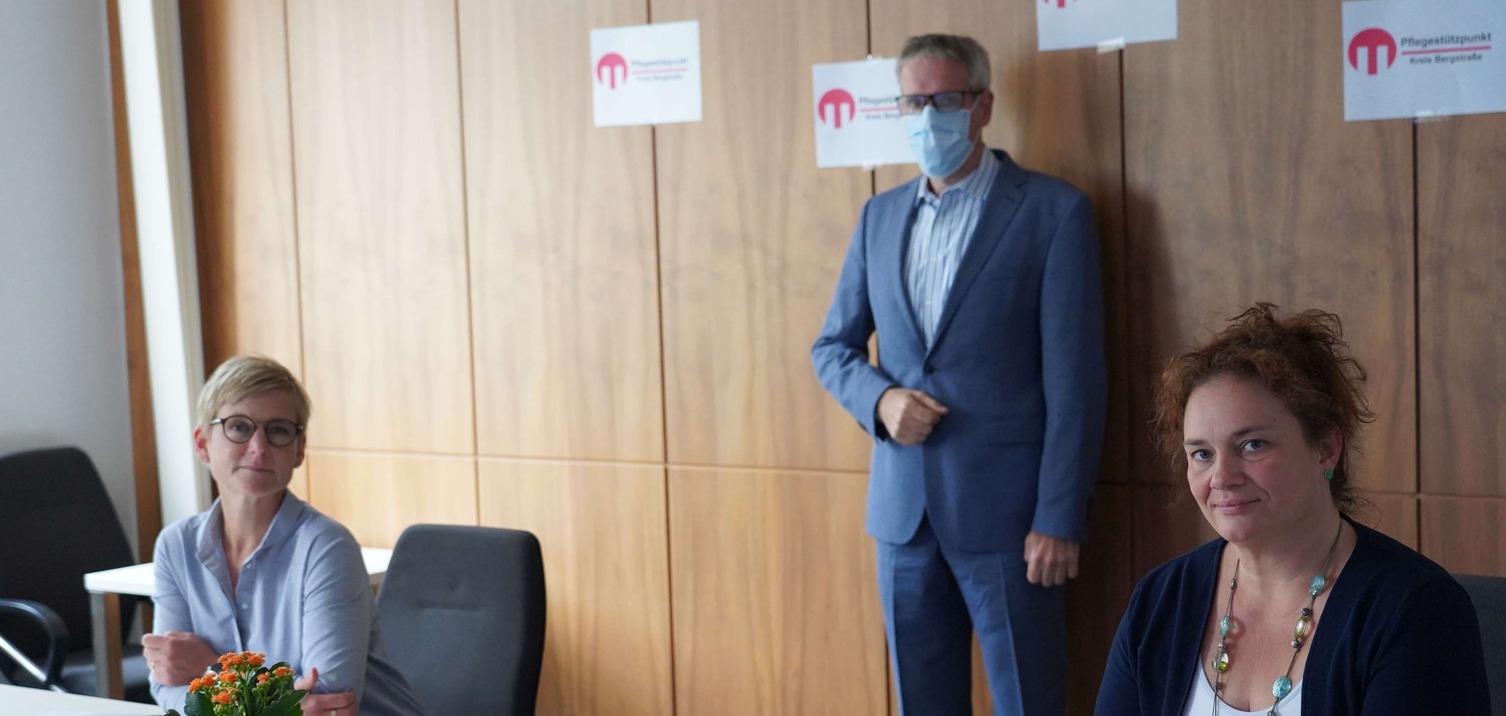 An einem weißen Tisch sitzen zwei Fragen, blond und brünett. in der Lücke zwischen den beiden Frauen, einen Schritt weiter hinten steht Landrat Christian Engelhardt.