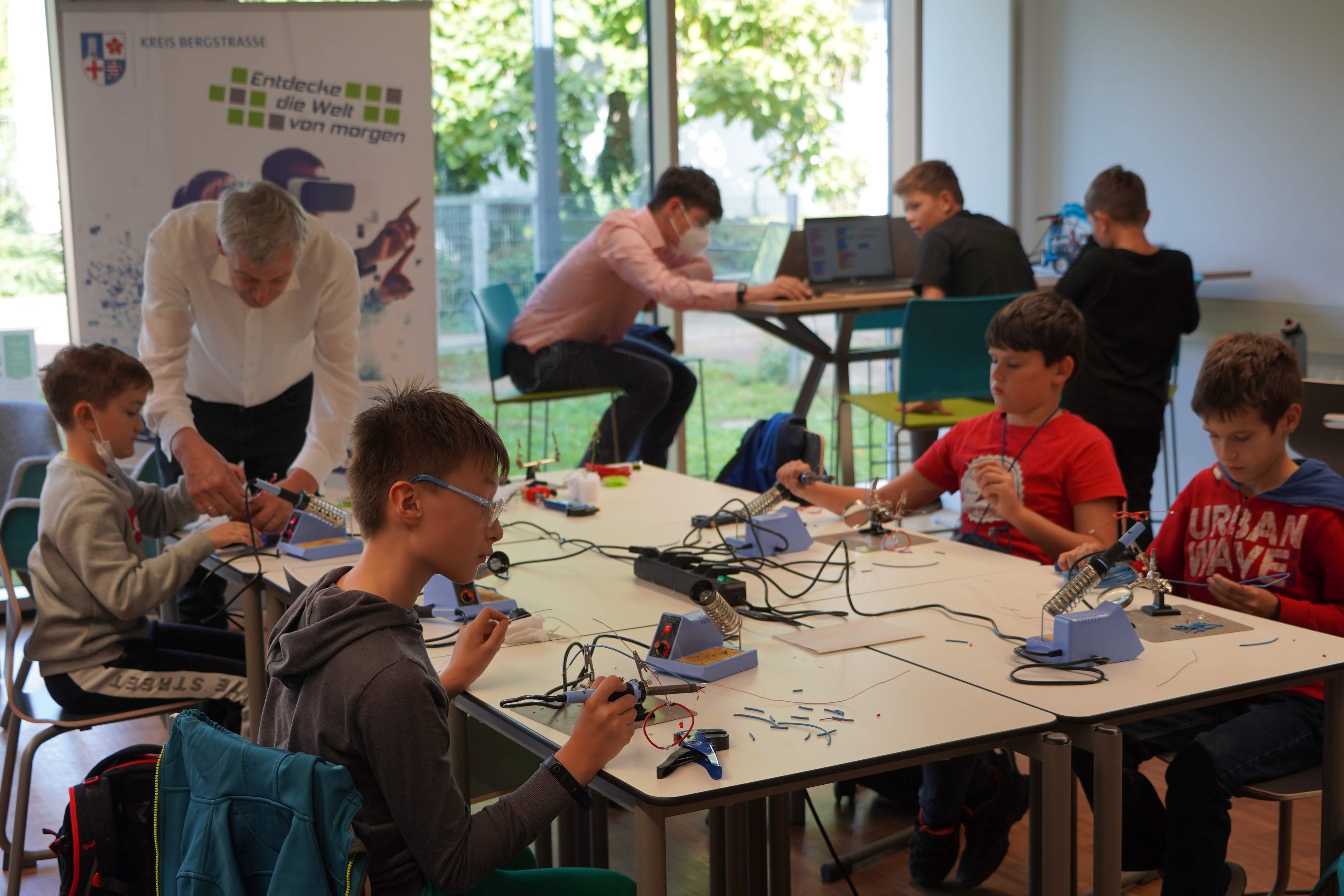 mehrere Schüler sitzen um einen Tisch herum und tüfteln.