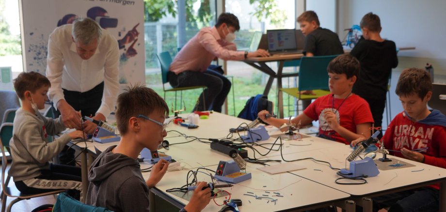 mehrere Schüler sitzen um einen Tisch herum und tüfteln.