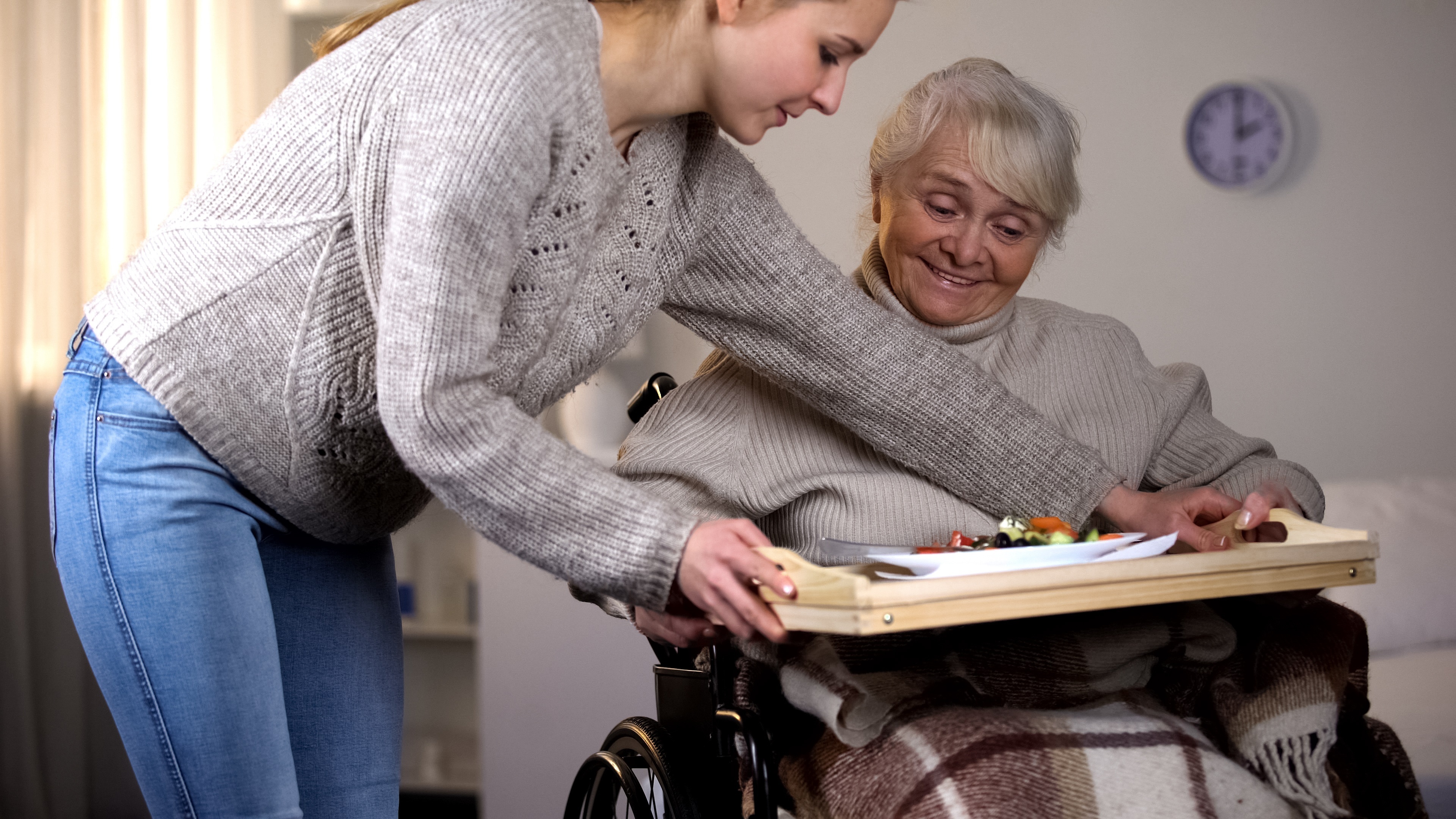 Helferin bringt Seniorin im Rollstuhl ein Essenstablett
