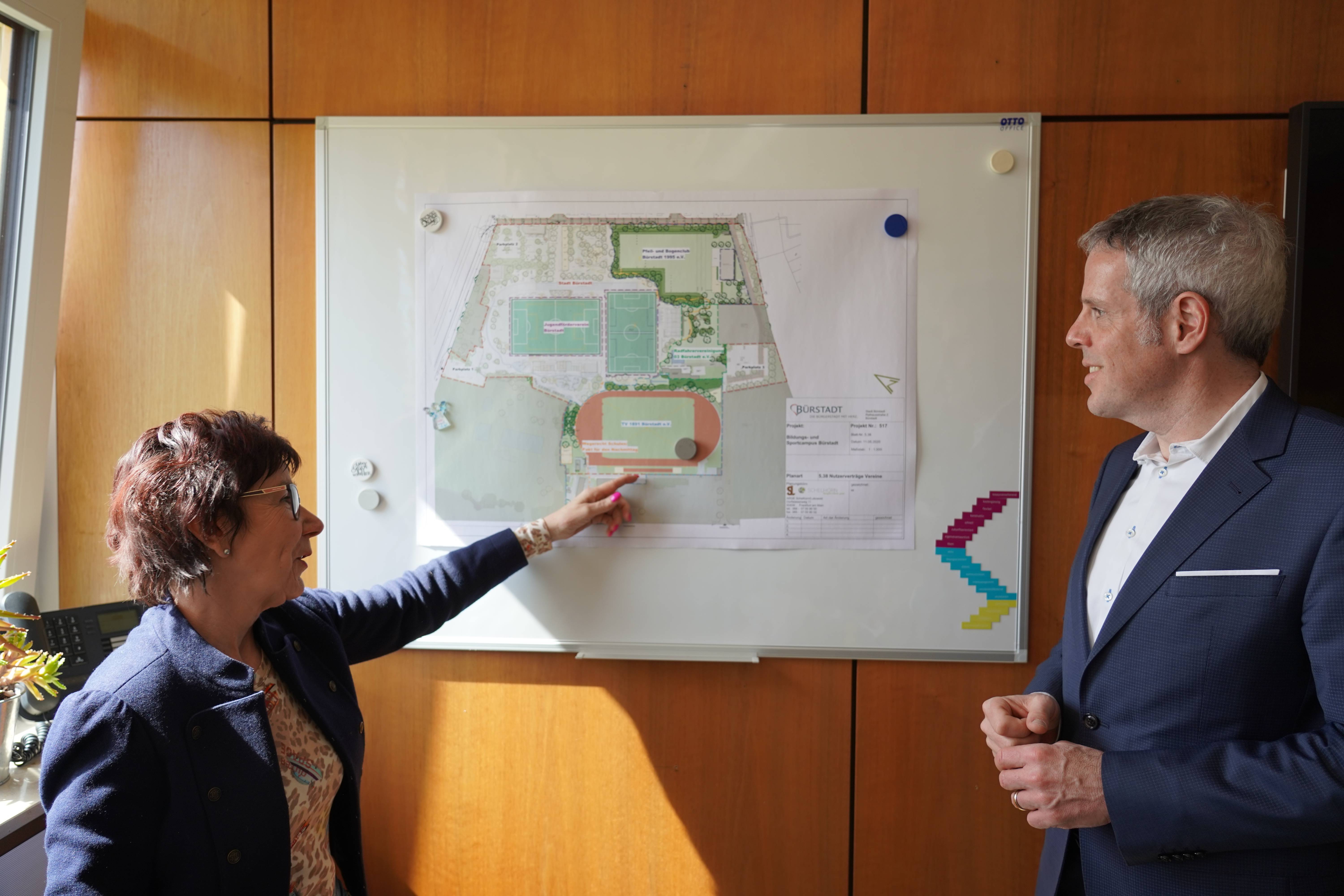 Landrat Christian Engelhardt und Bürgermeisterin Barbara Schader stehen im Bürstadter Rathaus vor einer Planungsunterlage. Die Bürgermeisterin zeigt dem Landrat etwas darauf. 