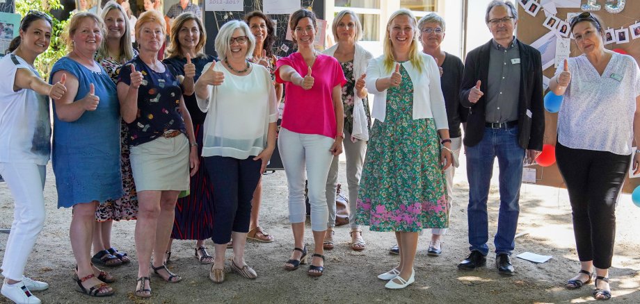 Das Bild zeigt die Erste Kreisbeigeordnete Diana Stolz (4. von rechts), den stellvertretenden Leiter des Fachbereiches Bildung, Betreuung und Erziehung im Jugendamt des Kreises Bergstraße Ulrich Schneider (2. von rechts) sowie die Leiterin des Fachbereiches Bildung, Betreuung und Erziehung Nicole Rothermel (rechts) mit den Mitarbeiterinnen von „Keiner fällt durchs Netz“ und der „Frühen Hilfen“. Sie stehen bei der Jubiläumsfeier des Projektes im Freien und zeigen den Daumen nach oben.