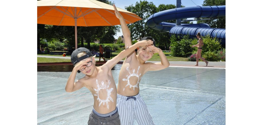 Zwei fröhliche Jungen im Freibad mit Sonnencreme-Sonnen auf dem Bauch