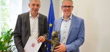 Landrat Christian Engelhardt (rechts) und der Referent für digitale Bildung des Kreises Bergstraße, Jan Fuchs (links), stehen gemeinsam im Büro des Landrates und freuen sich über den Bronzenen Löwen als Auszeichnung für den digi_space des Kreises beim Wettbewerb „Hessen smart gemacht“ der Hessischen Staatskanzlei und des Geschäftsbereichs der Ministerin für Digitale Strategie und Entwicklung. Der Landrat hält den Bronzenen Löwen in der Hand, Jan Fuchs die entsprechende Urkunde.