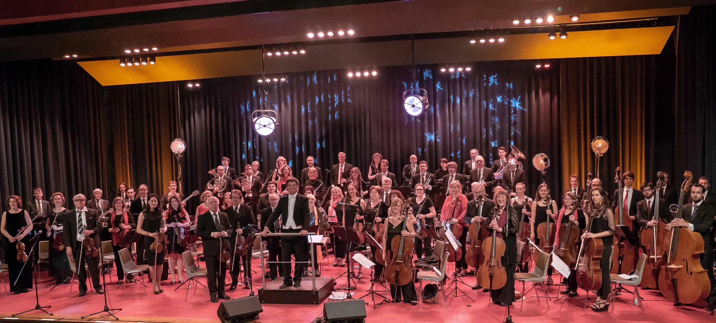 Das Bild zeigt das Orchester der Starkenburg Philharmoniker, das gesamte Orchester steht aufgereiht mit Instrumenten da und schaut in die Kamera.