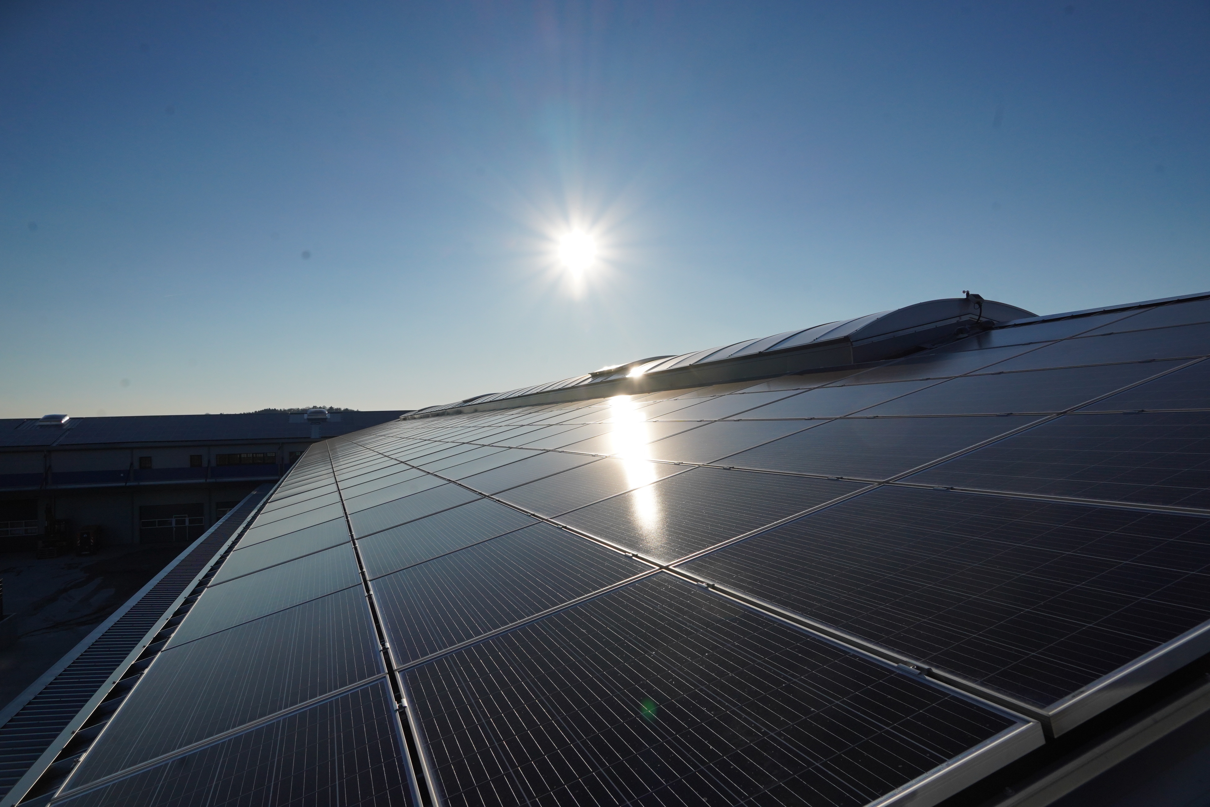 Die Sonne scheint auf ein mit vielen Photovoltaik-Modulen belegtes Dach.