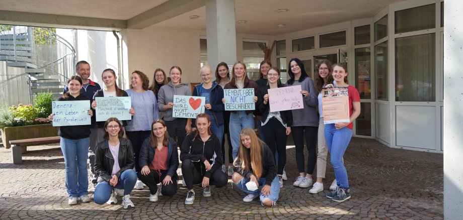 Schülerinnen der Liebfrauenschule in Bensheim stehen gemeinsam mit ihren Tutoren Dr. Nikolas Chalwatzis (2. von links) und Dr. Anette Grüttgen (5. von links) vor ihrer Schule und halten Plakate in die Höhe, die sich mit dem Thema Demenz auseinandersetzen. Darauf stehen Slogans wie etwa „Das Herz wird nicht dement“ oder „Demenz – manchmal sind es kleine Gesten, nicht große Worte“.