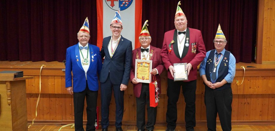 Im Zwingenberger Adlersaal steht Landrat Christian Engelhardt zusammen mit den von ihm geehrten Ernst Gerhard und MArkus Kropp sowie Ulrich Knorr und Siegmund Mendyk von NibA vor der Bühne. Alle tragen wie an Fastnacht üblich Narrenkappen.