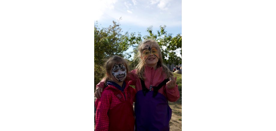 Zwei Kinder mit angemalten Gesichtern, eines als Zebra, das andere als Schmetterling, lachen in die Kamera.