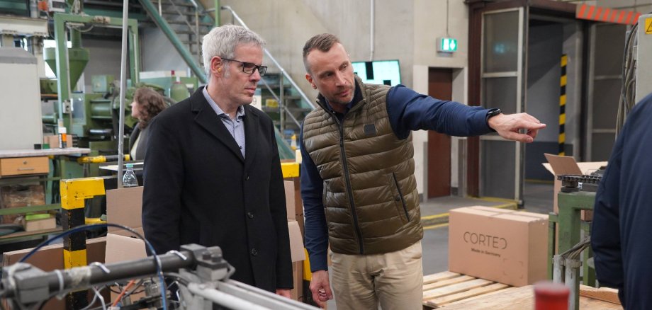 Geschäftsführer Torsten Schmitt (links) zeigt Landrat Christian Engelhardt (rechts) wie die nachhaltigen Kleiderbügel in Wahlen produziert werden.