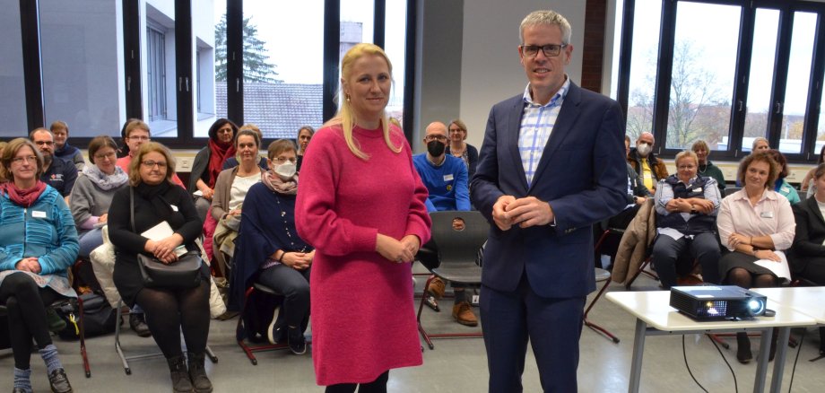 Landrat Christian Engelhardt und die Erster Kreisbeigeordnete Diana Stolz stehen auf dem Foto vor den Teilnehmerinnen und Teilnehmern des Pflegetisches, die im Hintergrund sitzen.