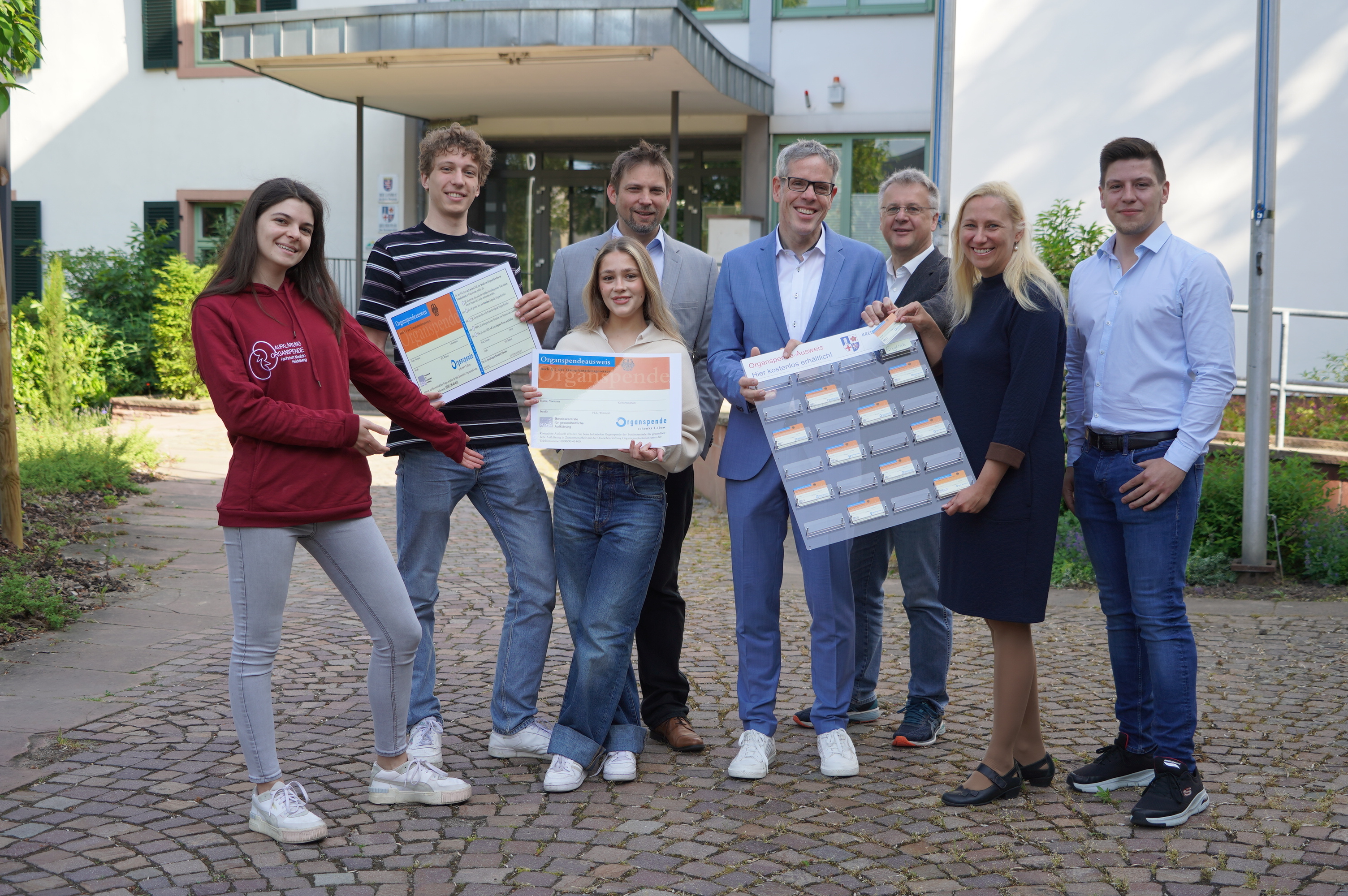 Die Erste Kreisbeigeordnete Diana Stolz (2. v. rechts) überreichte eine Organspendeausweis-Tafel an Landrat und Personalchef Christian Engelhardt (4. v. rechts). Diese hängt nun bereits im Neuen Landratsamt. Mit dabei (von links nach rechts): Sarah Reudenbach, Ole Knöller und Tami Gibson von der Lokalgruppe Organspende der Universität Heidelberg, Prof. Dr. med. Phillip Knebel (Chefarzt Allgemein- und Viszeralchirurgie am Kreiskrankenhaus Bergstraße), Heppenheims Bürgermeister Rainer Burelbach und Knochenmarkspender Florian Hofmann.
