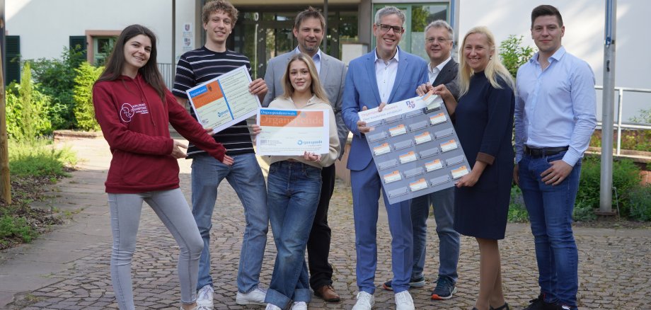 Die Erste Kreisbeigeordnete Diana Stolz (2. v. rechts) überreichte eine Organspendeausweis-Tafel an Landrat und Personalchef Christian Engelhardt (4. v. rechts). Diese hängt nun bereits im Neuen Landratsamt. Mit dabei (von links nach rechts): Sarah Reudenbach, Ole Knöller und Tami Gibson von der Lokalgruppe Organspende der Universität Heidelberg, Prof. Dr. med. Phillip Knebel (Chefarzt Allgemein- und Viszeralchirurgie am Kreiskrankenhaus Bergstraße), Heppenheims Bürgermeister Rainer Burelbach und Knochenmarkspender Florian Hofmann.