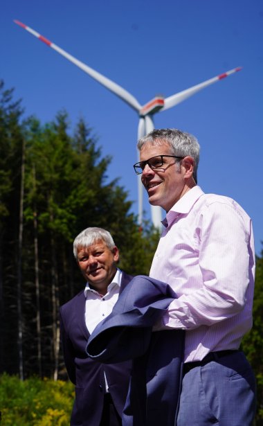 Landrat Christian Engelhardt (rechts) informierte sich bei Bürgermeister Volker Oehlenschläger (links) über die Effizienz der Windräder am Kahlberg. Auf dem Bild sind beide im Wald vor einem der Windräder zu sehen.