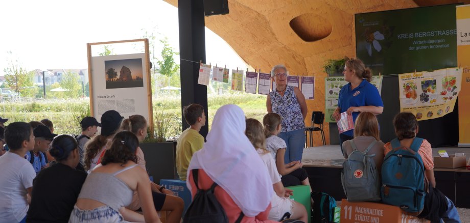 Frau Billau, die Vorsitzende des Bezirkslandfrauenvereins Heppenheim steht vor den Schülerinnen und Schülern der Alfred-Delp-Schule und weist diese in den Ablauf der "Zukunft schmeckt - regional, nachhaltig“-Mitmachaktion ein.