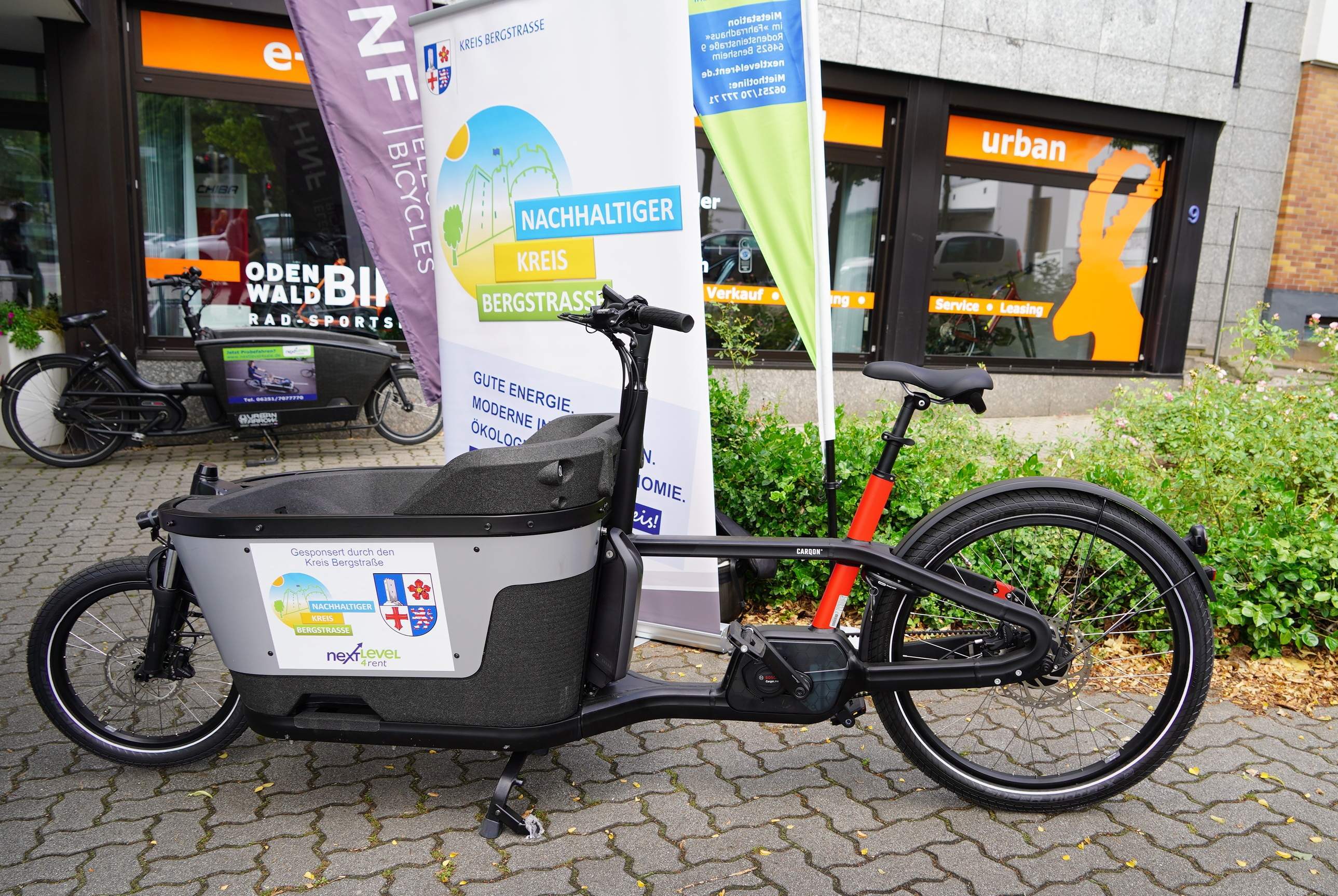 Das E-Lastenrad von der next level GmbH steht vor einem Aufsteller des Kreises Bergstraße.