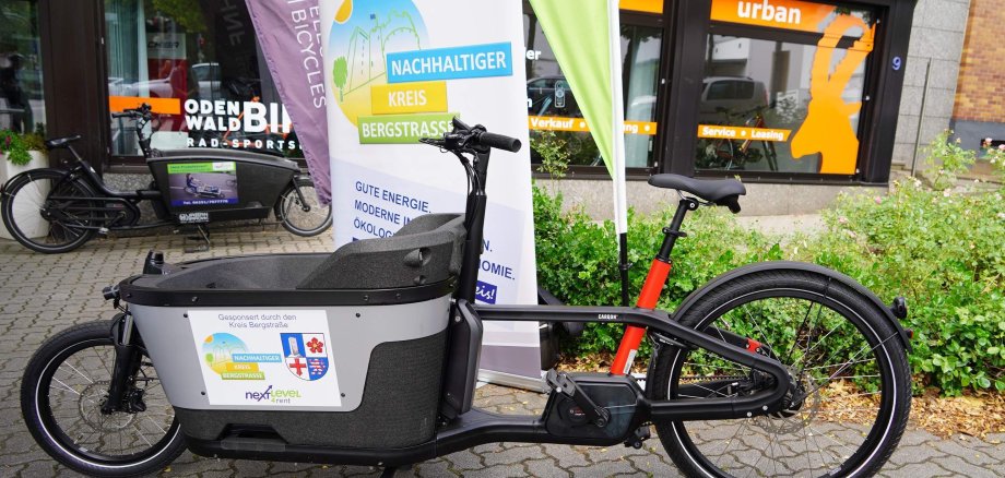 Das E-Lastenrad von der next level GmbH steht vor einem Aufsteller des Kreises Bergstraße.