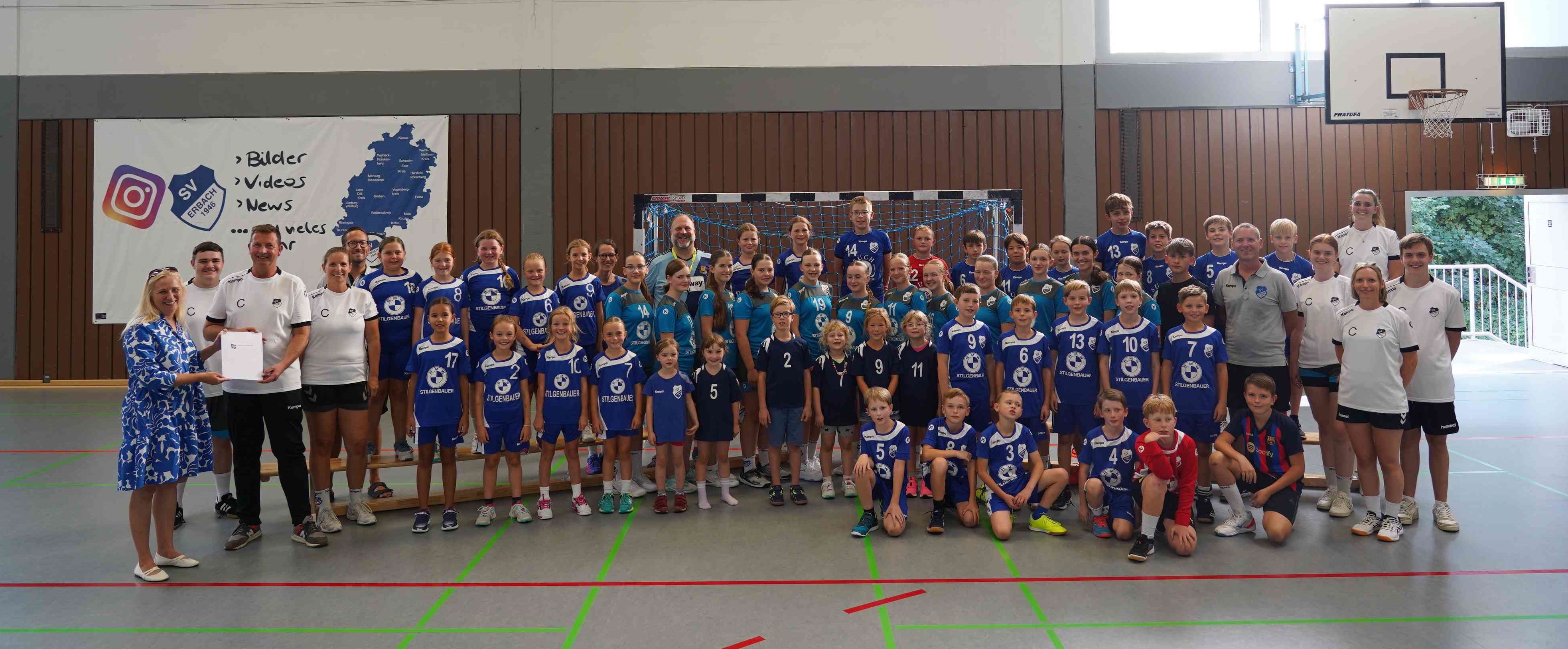Die Erste Kreisbeigeordnete und Jugenddezernentin Diana Stolz mit dem Jugendleiter des SV Erbachs, Thomas Bernhardt, den Jugendtrainerinnen und -trainern sowie Jugendbetreuerinnen und -betreuern und den großen und kleinen Handballerinnen und Handballern des Vereins. 
