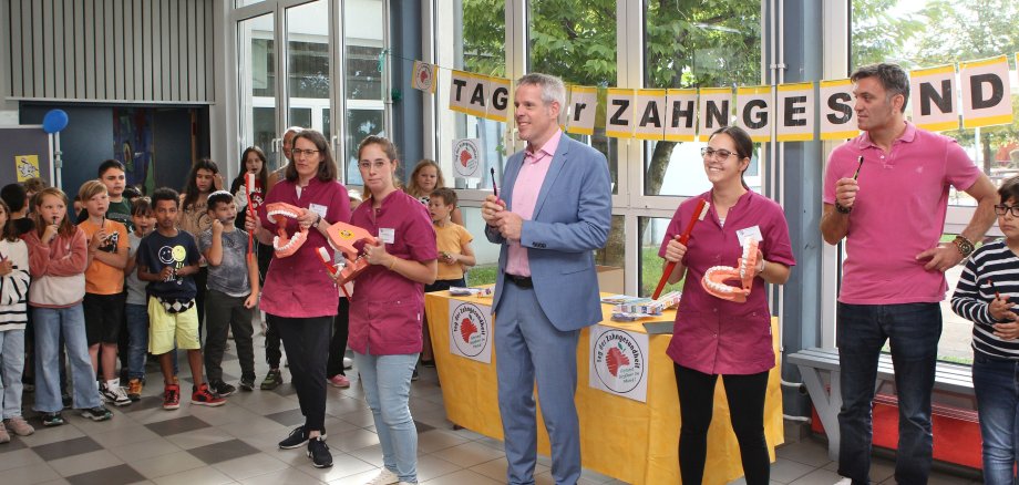 Landrat Christian Engelhardt (3. v. re.), der Leiter der Friedrich-Fröbel-Schule Viernheim Markus Taube (ganz rechts) und die Mitarbeiterinnen des Zahnärztlichen Dienstes des Bergsträßer Gesundheitsamtes übten mit den Drittklässlerinnen und Drittklässlern beim „Zahnputz-Rap“ das korrekte Zähneputzen.