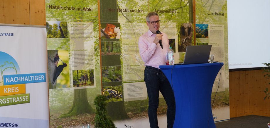 Landrat Christian Engelhardt steht, mit einem Mikrofon in der Hand, auf einer und begrüßt die Besucherinnen und Besucher des 2. Klimaforums Bergstraße.