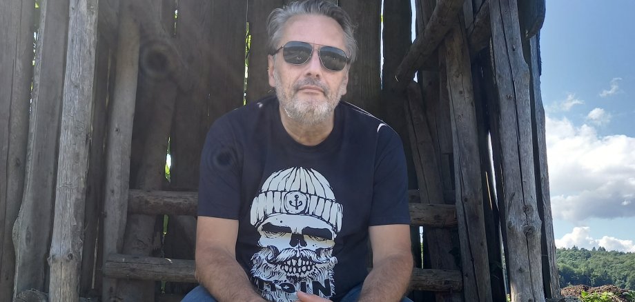 Der Künstler Alexander Romanowicz sitzt im Freien auf einem Ansitzeinrichtung.