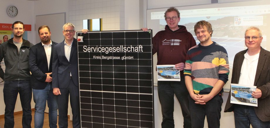 Landrat Christian Engelhardt, der Geschäftsführer der Servicegesellschaft Kreis Bergstraße, Marc Colin, Sebastian Beiwinkel und Marc Schmiedel von der ausführenden Firma PBS Energie GmbH sowie der Schulleiter der EBS, Christian Mang und der stellvertretende Schulleiter des ÜWGs, Ekkehard Müller stehen neben einer PV-Anlage. 