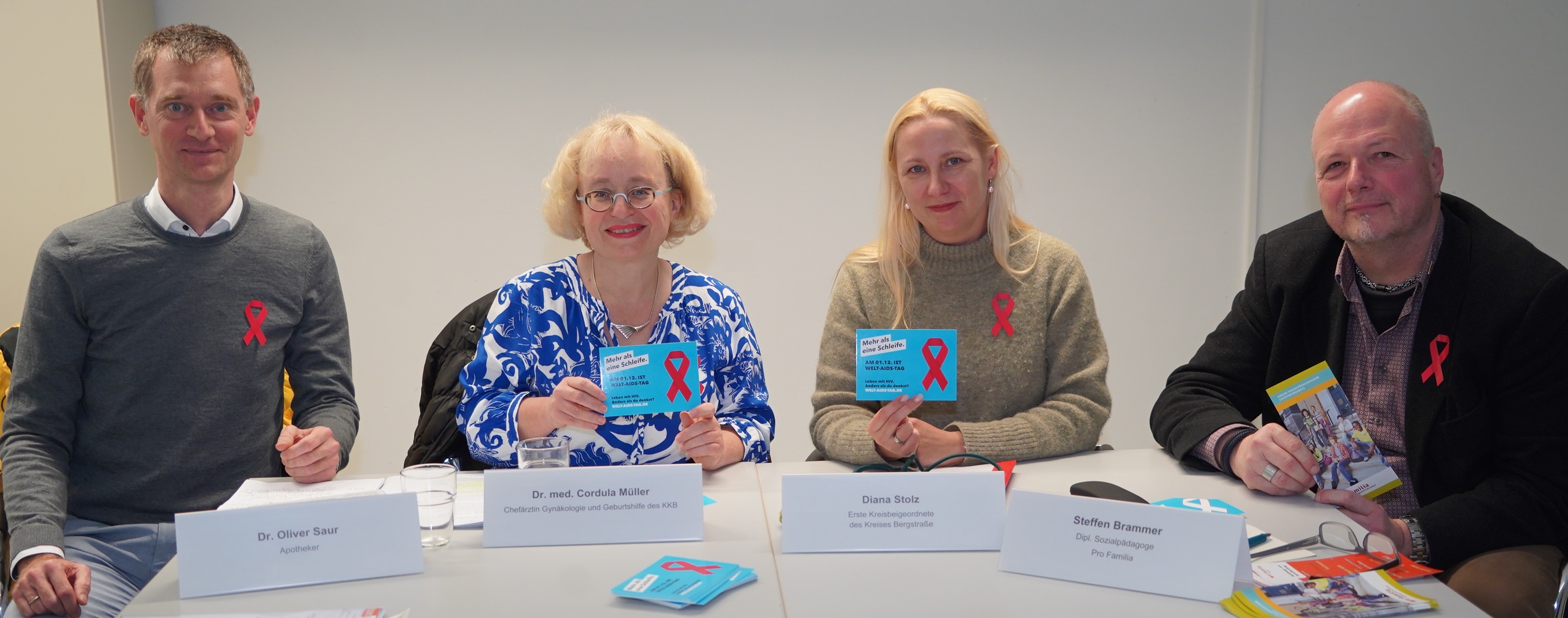 Die Erste Kreisbeigeordnete und Gesundheitsdezernentin Diana Stolz, die Chefärztin für Gynäkologie und Geburtshilfe des KKB, Dr. Cordula Müller, der Sozial- und Sexualpädagoge Steffen Brammer von pro familia Bensheim und der Apotheker Dr. Oliver Saur sitzen an einem Tisch und halten Informationsflyer zum Thema HIV und AIDS in den Händen.