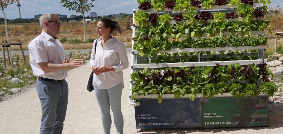 Landrat Christian Engelhardt steht gemeinsam mit der Mitgründerin Dr. Julia Dubowy vor der Pflanzentheke auf der Bundesgartenschau in Mannheim und lässt sich erklären, wie das Projekt die Landwirtschaft verändern will.