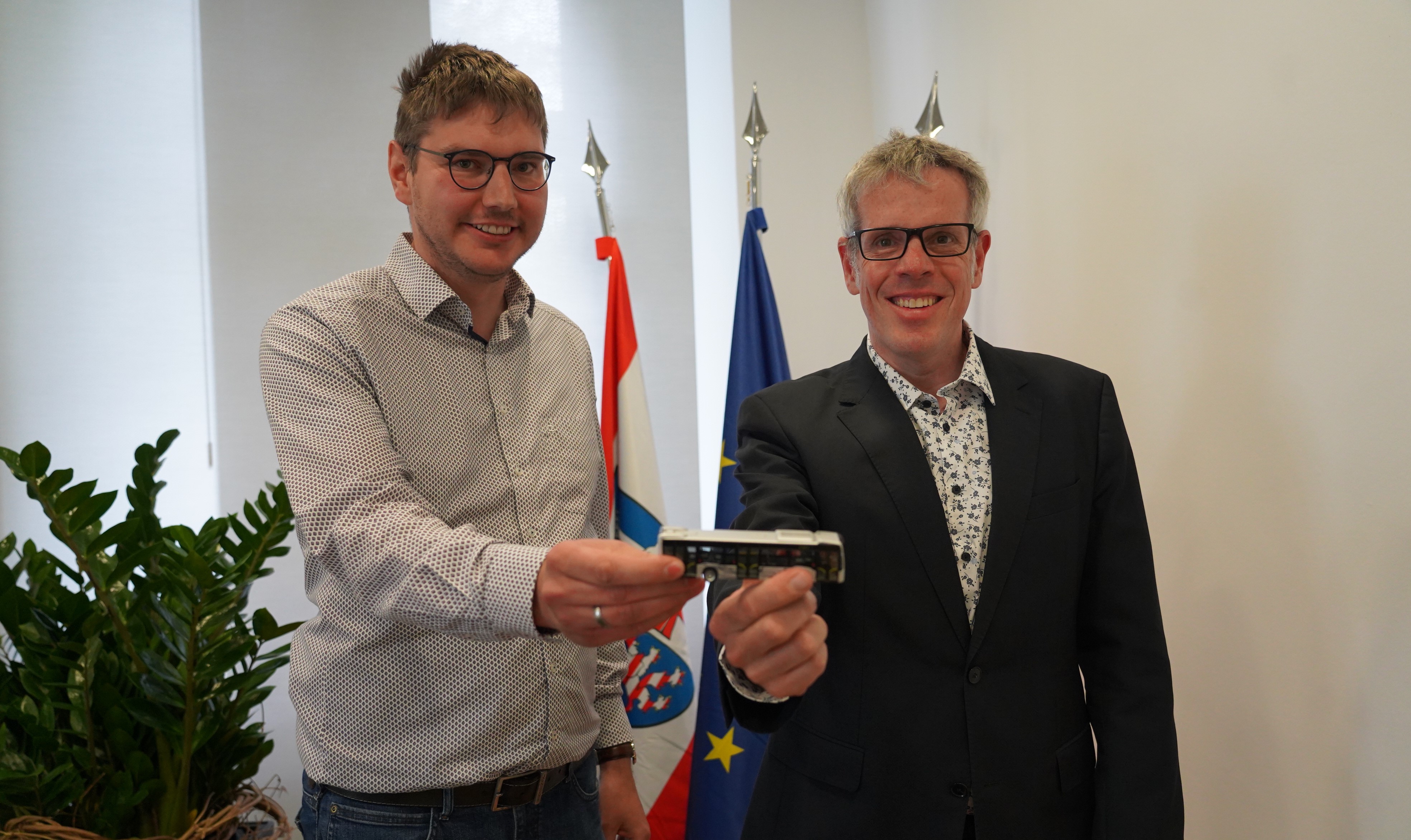 Der neue Abteilungsleiter für ÖPNV und Mobilität Dominik Perleth und Landrat Christian Engelhardt halten gemeinsam einen kleinen Spielzeugbus in die Kamera.
