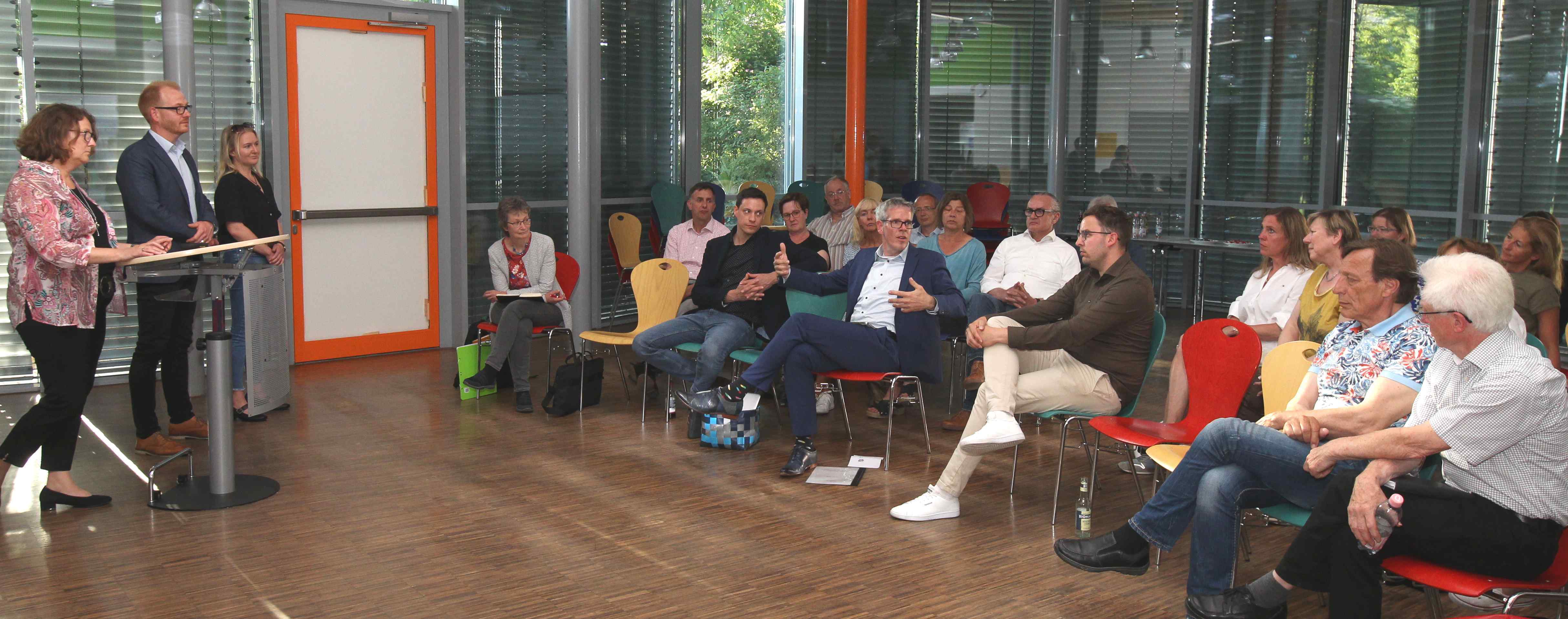 Landrat Christian Engelhardt sitzt mit Karin Doberer von LernLandSchaft, dem Technischen Betriebsleiter des Eigenbetriebs Schule und Gebäudewirtschaft, Johannes Kühn, und der zuständigen Projektleiterin, Caroline Barthelmes, in einem Besprechungssaal und präsentiert weiteren Teilnehmerinnen und Teilnehmeren die weiteren Schritte zur neuen Schule in Viernheim.