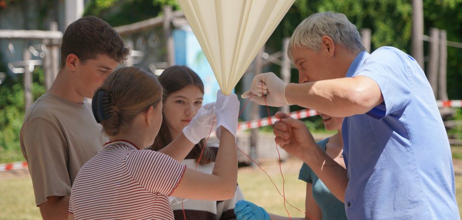 Die Schülerinnen und Schüler des Naturwissenschaftskurses, Kurslehrerin Eva Nagel und der Referent für digitale Bildung und Leiter des digi_space des Kreises Bergstraße Jan Fuchs halten gemeinsam den mit Helium gefüllten, weißen Ballon und befestigen mit einer roten Kordel die Sonde.