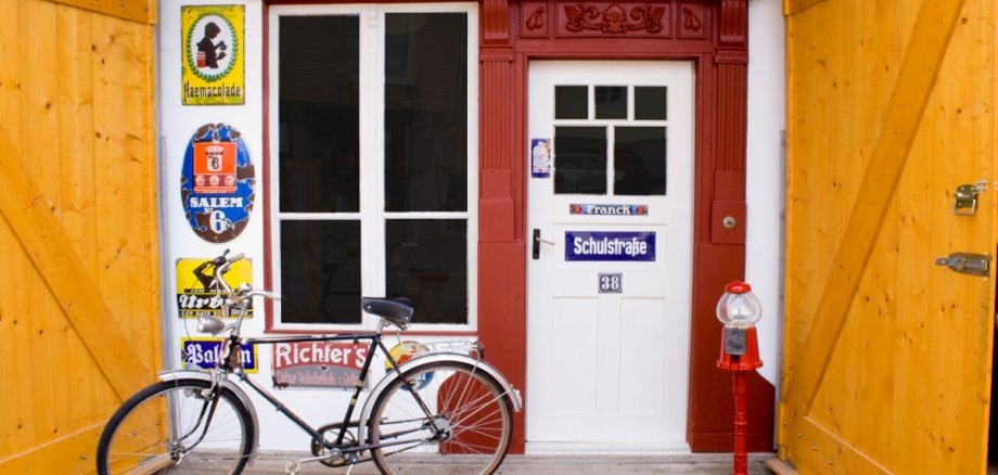 Der Eingang des Museum: Neben der weißen Holztür hängen alte Schilder und ein Fahrrad steht davor.