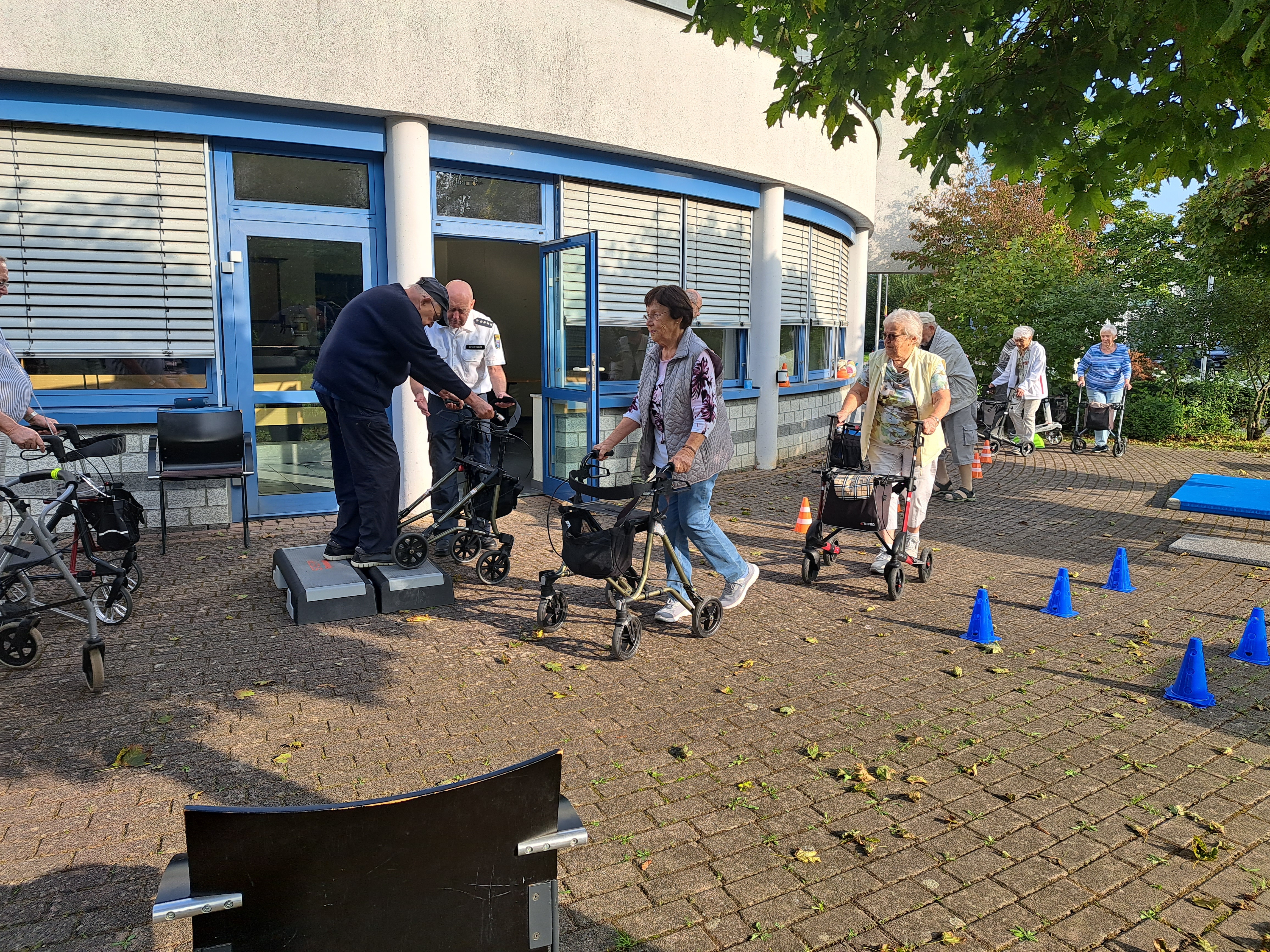 Ein paar Seniorinnen und Senioren laufen mit ihren Rollatoren bei einem Rollator-Training durch einen Parcours.