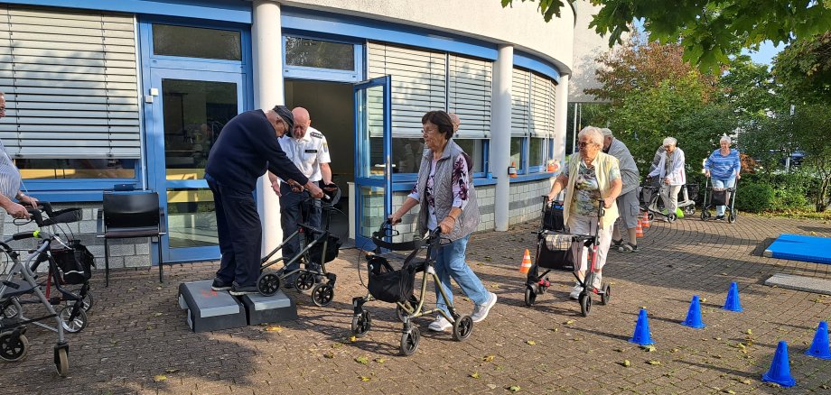 Ein paar Seniorinnen und Senioren laufen mit ihren Rollatoren bei einem Rollator-Training durch einen Parcours.