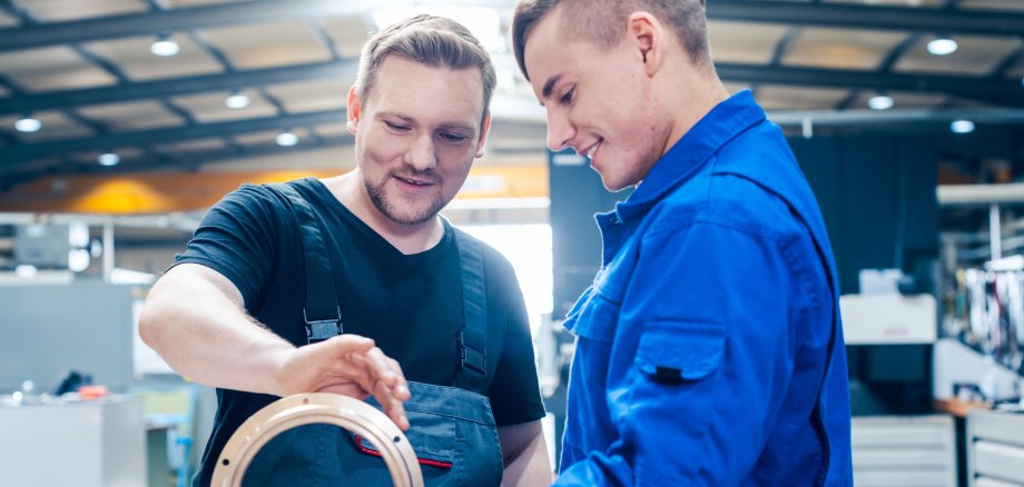 Auf dem Symbolfoto bespricht ein Ausbilder mit einem Auszubildenden im Blaumann ein Werkstück aus dem Bereich Metallbau/Maschinenbau.