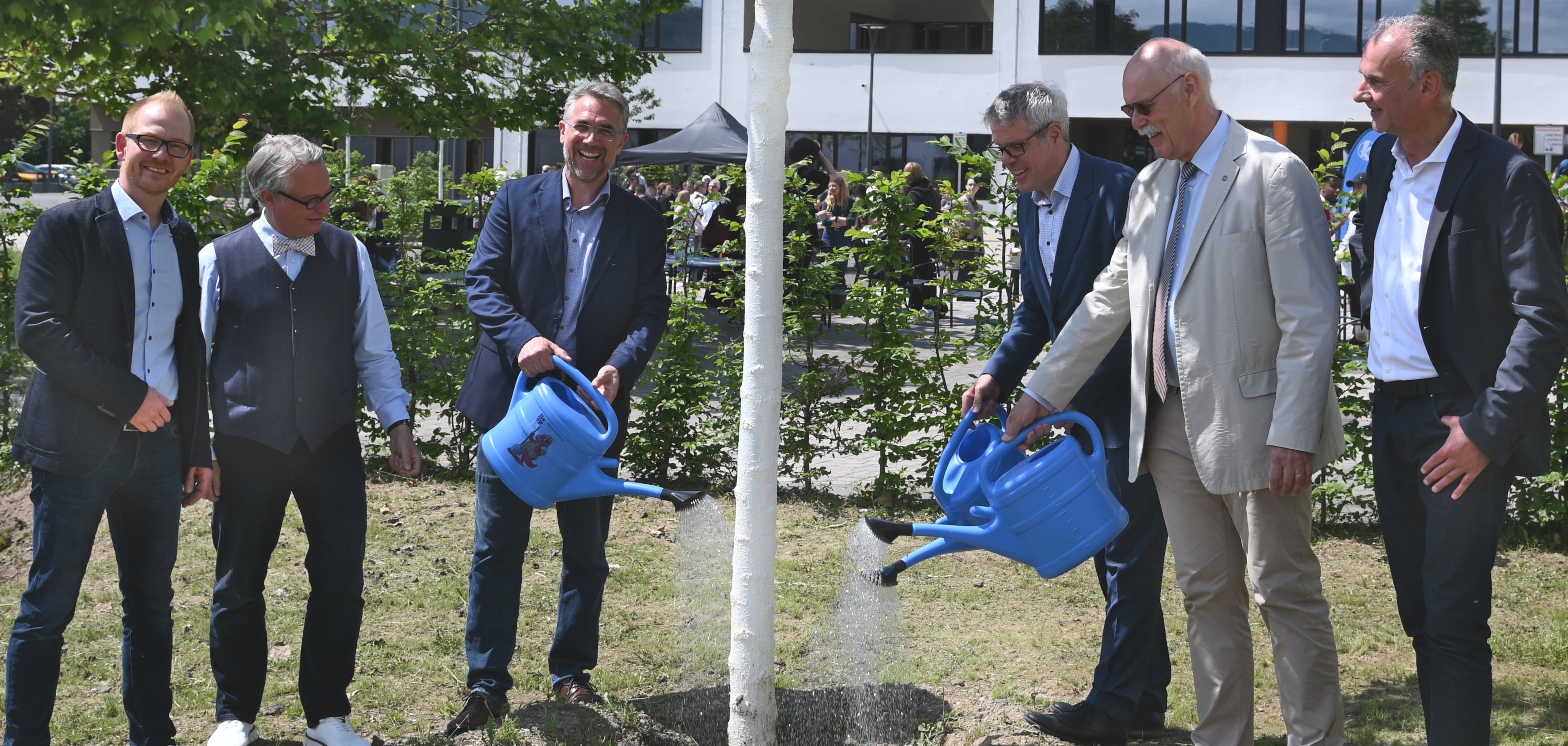 Johannes Kühn, Dr. Ulrich Kuther von der Karl Kübel Stiftung, Michael Steffan, Landrat Christian Engelhardt, Peter Born und Martin Rieger stehen auf dem neuen Außengelände und gießen gemeinsam einen Baum.