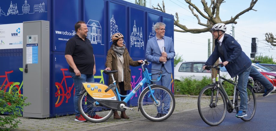 Landrat Christian Engelhardt steht mit der in der Kreisverwaltung für den Radverkehr zuständigen Sachbearbeiterin Lisa-Marie Riemann, dem Bürgermeister von Heppenheim, Rainer Burelbach und Michael Lortz vom Fachbereich Stadtmarketing der Stadt Heppenheim vor einer VRN-Bikebox..