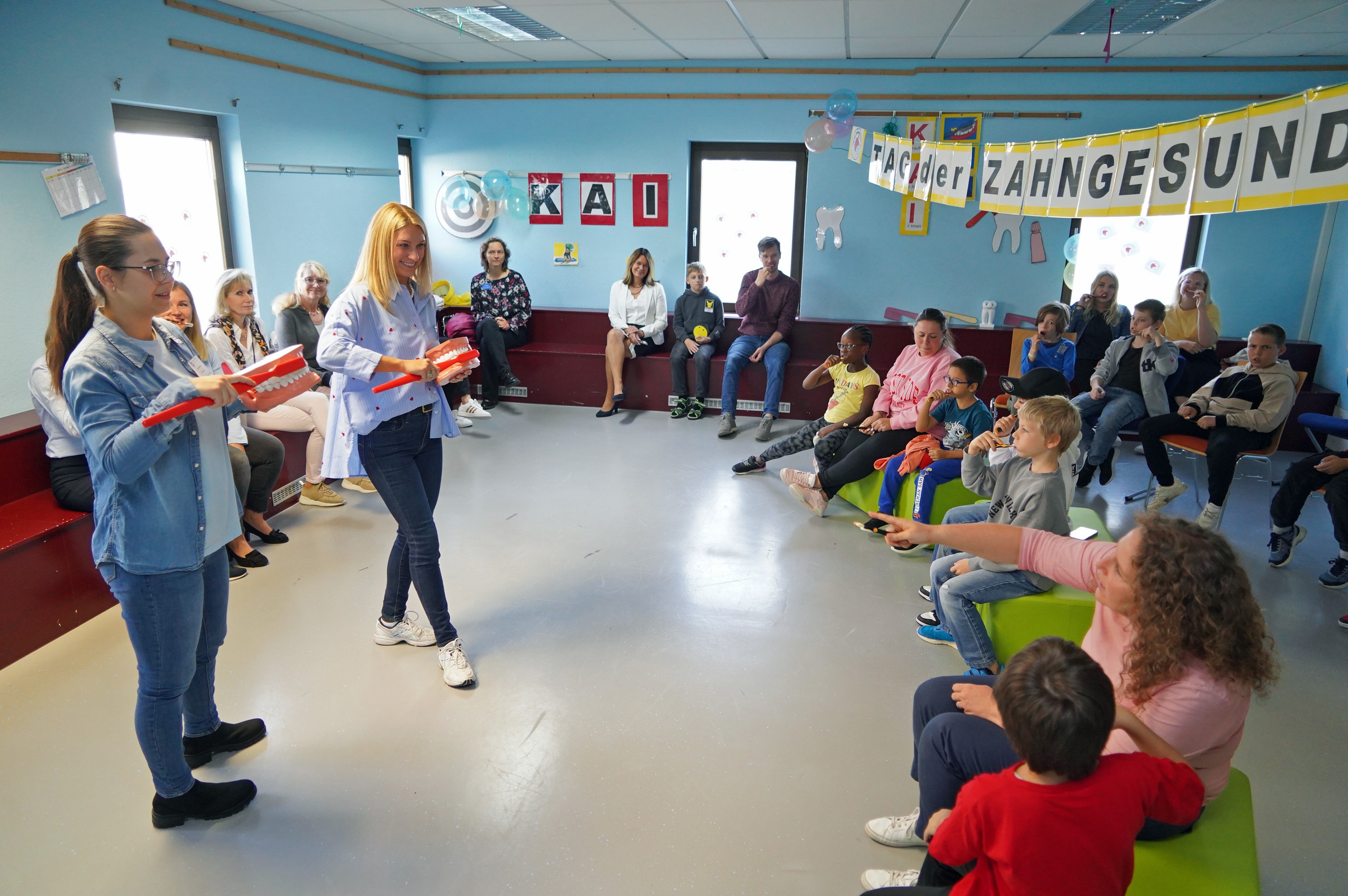 Die Mitarbeiterinnen des Zahnärztlichen Dienstes des Bergsträßer Gesundheitsamtes Michelle Reinhart und Anastasia Simon und die Erste Kreisbeigeordnete Angelika Beckenbach (Bildmitte) demonstrierten beim Zahnputz-Rap gemeinsam mit den Schülerinnen und Schülern der Bensheimer Weschnitztalschule, wie richtiges Zähneputzen funktioniert. Dazu haben die Gesundheitsamt-Mitarbeiterinnen zwei große Plastik-Gebisse und eine überdimensionale Zahnbürste in der Hand.