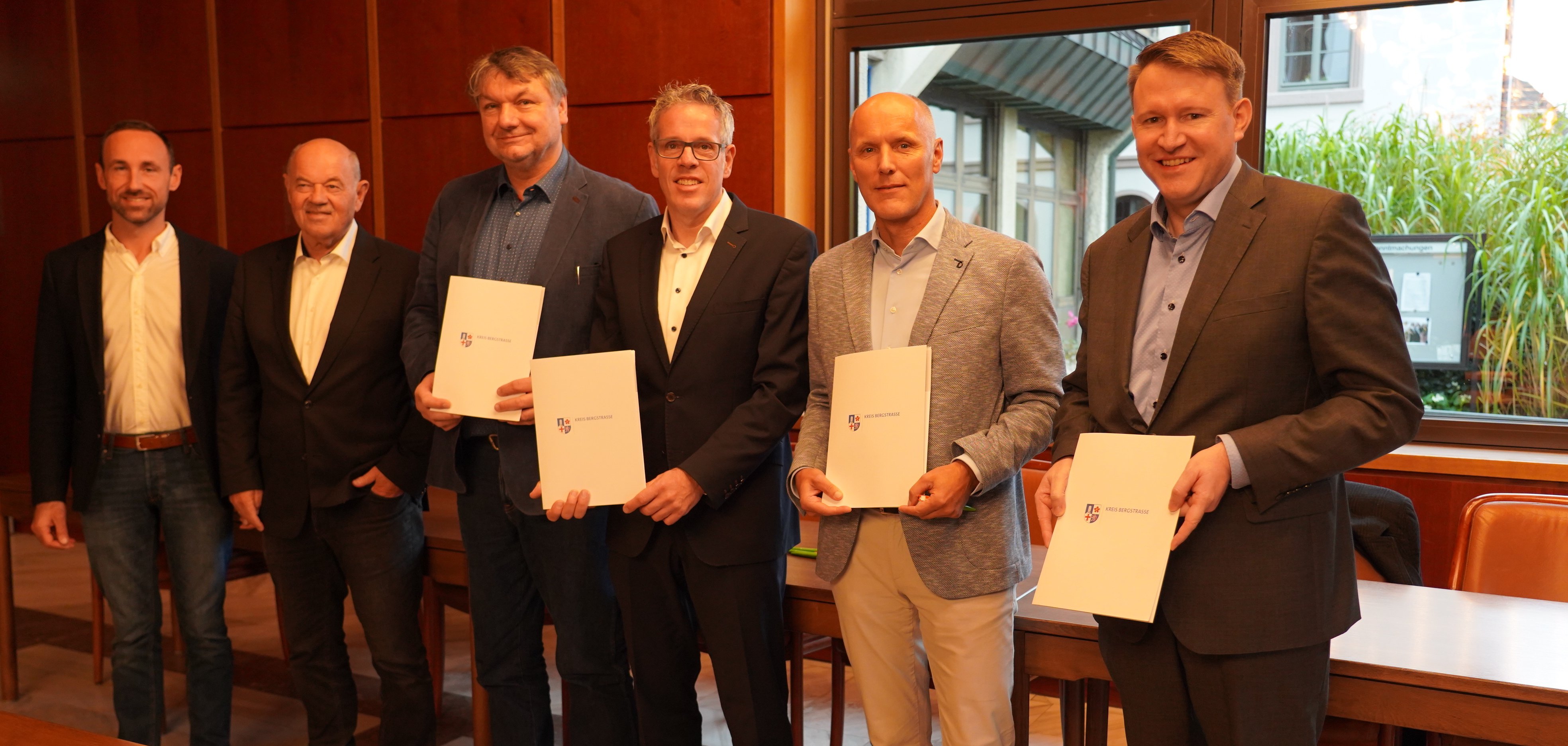 Der Vorsitzende der Gemeindevertretung Biblis, Konstantin Großmann, der Erste Beigeordnete des Gemeindevorstands Biblis, Herbert Ritzert, der Bürgermeister der Gemeinde Biblis, Volker Scheib, Landrat Christian Engelhardt, der Leiter der Rückbauanlage Biblis, Ralf Stüwe vom Energieversorgungskonzern RWE nuclear GmbH sowie der Geschäftsführer der Wirtschaftsförderung Bergstraße, Dr. Matthias Zürker stehen in einem Sitzungssaal des Bibliser Rathaus nebeneinander und halten die unterzeichneten Kooperationsvereinbarung in den Händen.