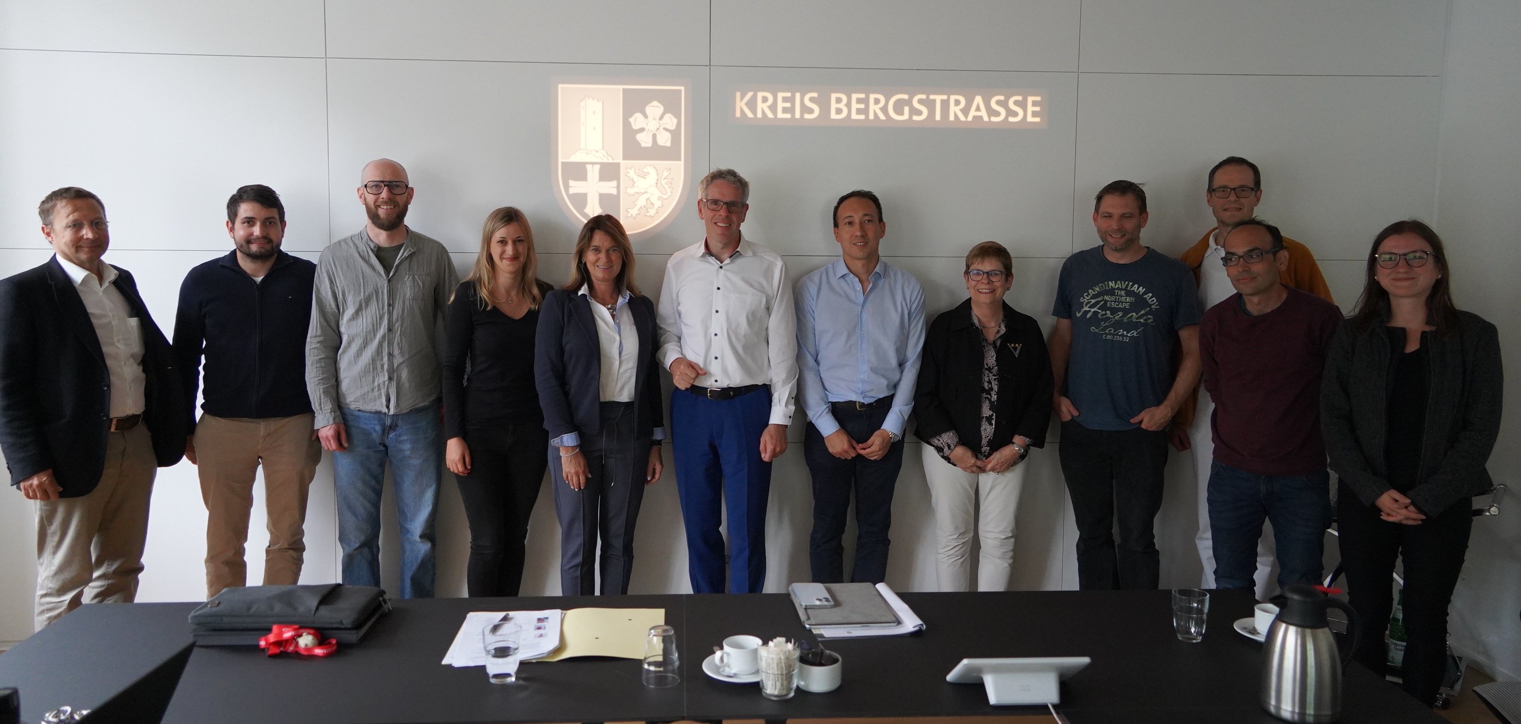 Landrat Christian Engelhardt und die Erste Kreisbeigeordnete Angelika Beckenbach stehen mit den Teilnehmerinnen und Teilnehmern des jüngsten Treffens des Weiterbildungsverbandes Allgemeinmedizin Bergstraße im Nibelungensaal des Landratsamts vor einer Wand mit dem Kreislogo.