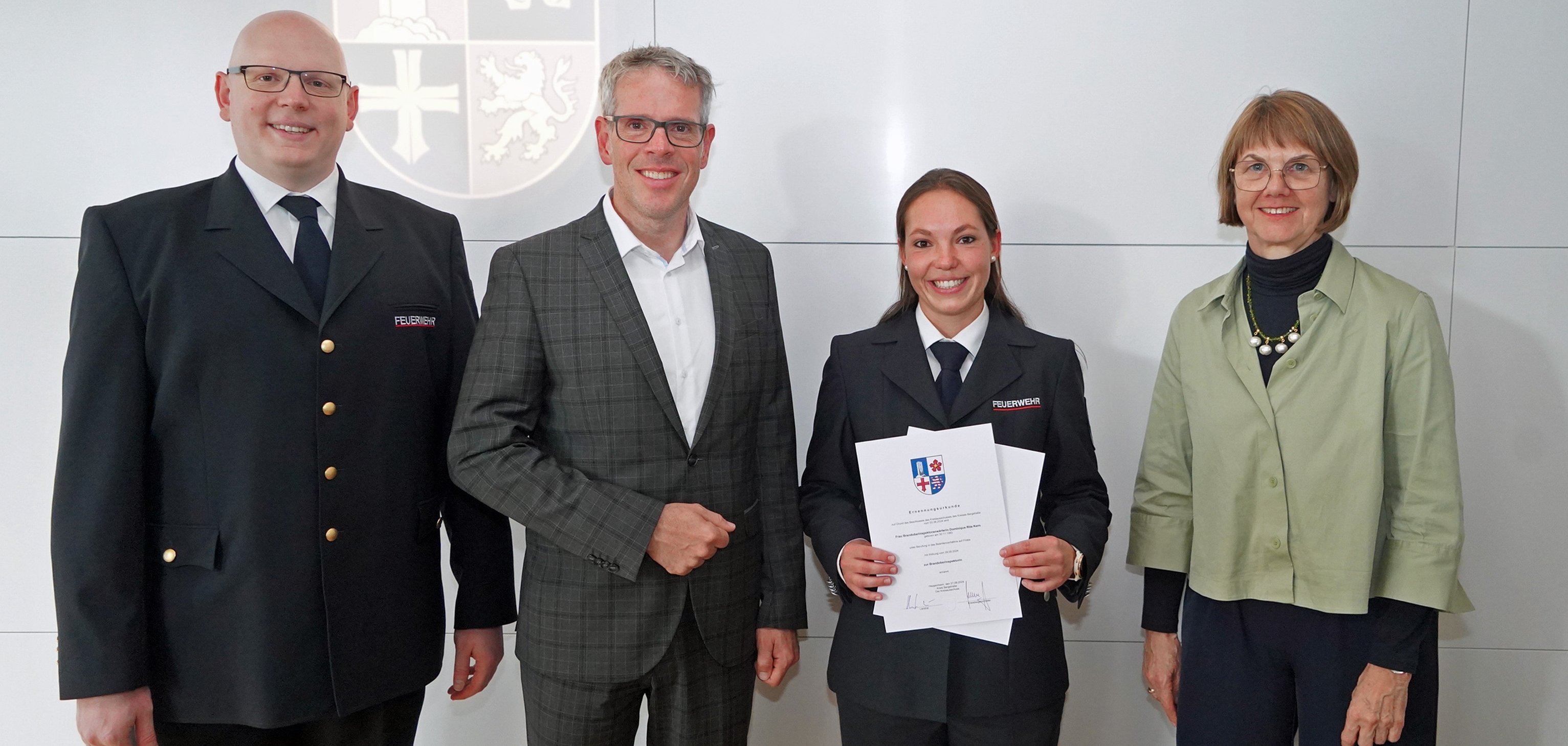 Landrat Christian Engelhardt, Dominique Kern, Markus Stracke, stellvertretender Leiter der Abteilung Gefahrenabwehr, und Barbara Hoffbauer, Leiterin der Abteilung Personalmanagement und Organisation stehen im Heppenheimer Landratsamt vor einer Wand. Frau Brand hält ihre Urkunde in den Händen.