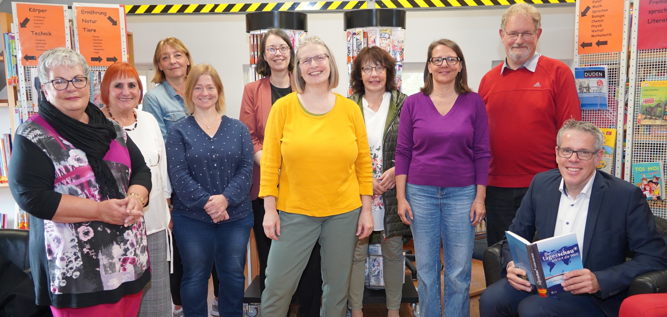 Landrat Christian Engelhardt sitzt mit den Vertreterinnen und Vertretern der Bibliotheken des Kreises zum beim Pressegespräch vor Bücherregalen in der Stadtbücherei Heppenheim.