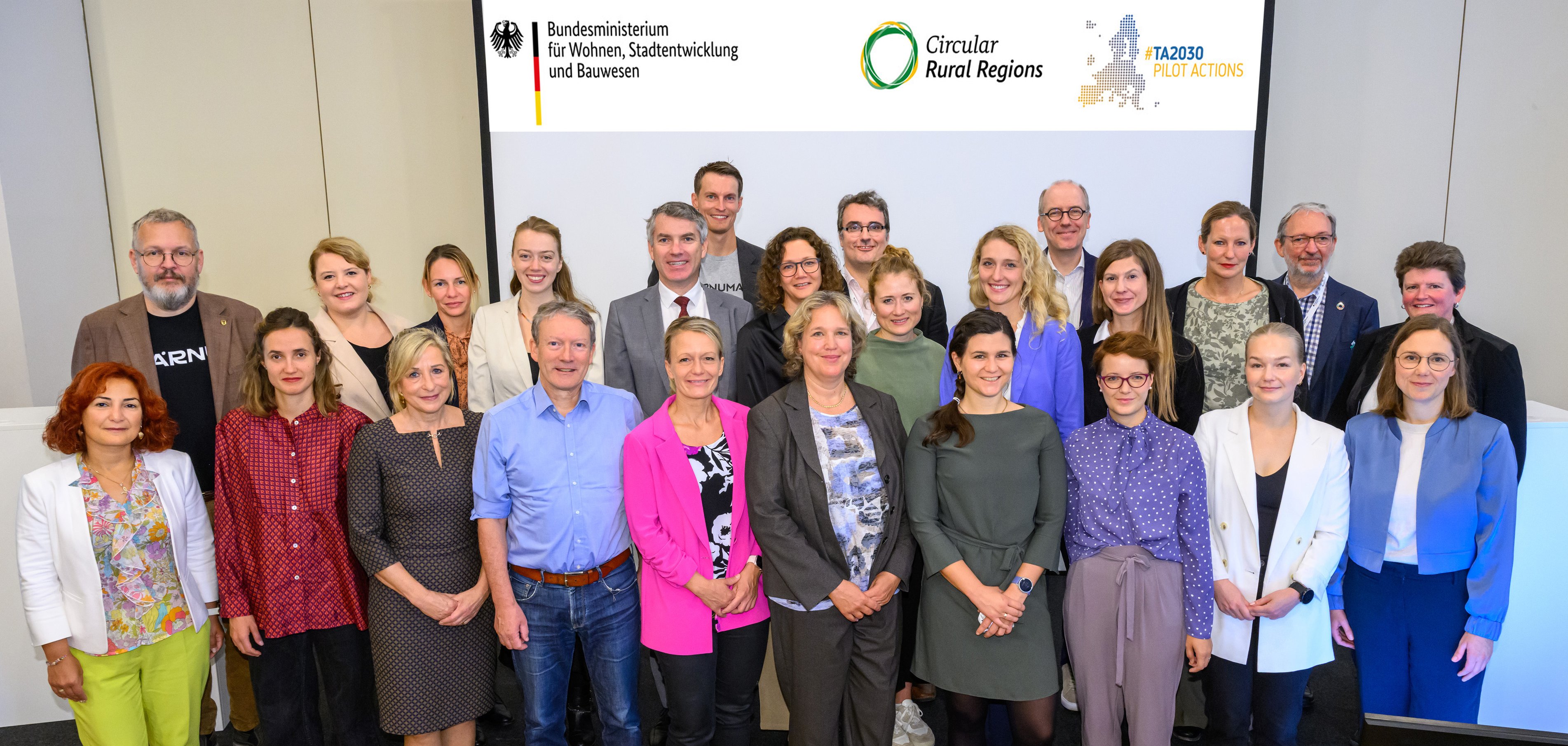 Die Teilnehmenden aus den fünf deutschen und europäischen Metropolregionen stehen bei der Auftaktkonferenz in Berlin vor einem Whiteboard.