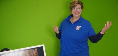Ute Fuchs, Mitarbeiterin des Bergsträßer Gesundheitsamts, steht vor einem Greenscreen und demonstriert die Möglichkeit zur digitalen Videosprechstunde.