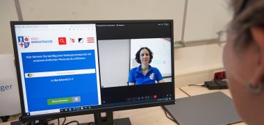 Eine Mitarbeiterin des Gesundheitsamtes sitzt vor einem PC und demonstriert die Terminvereinbarung online.